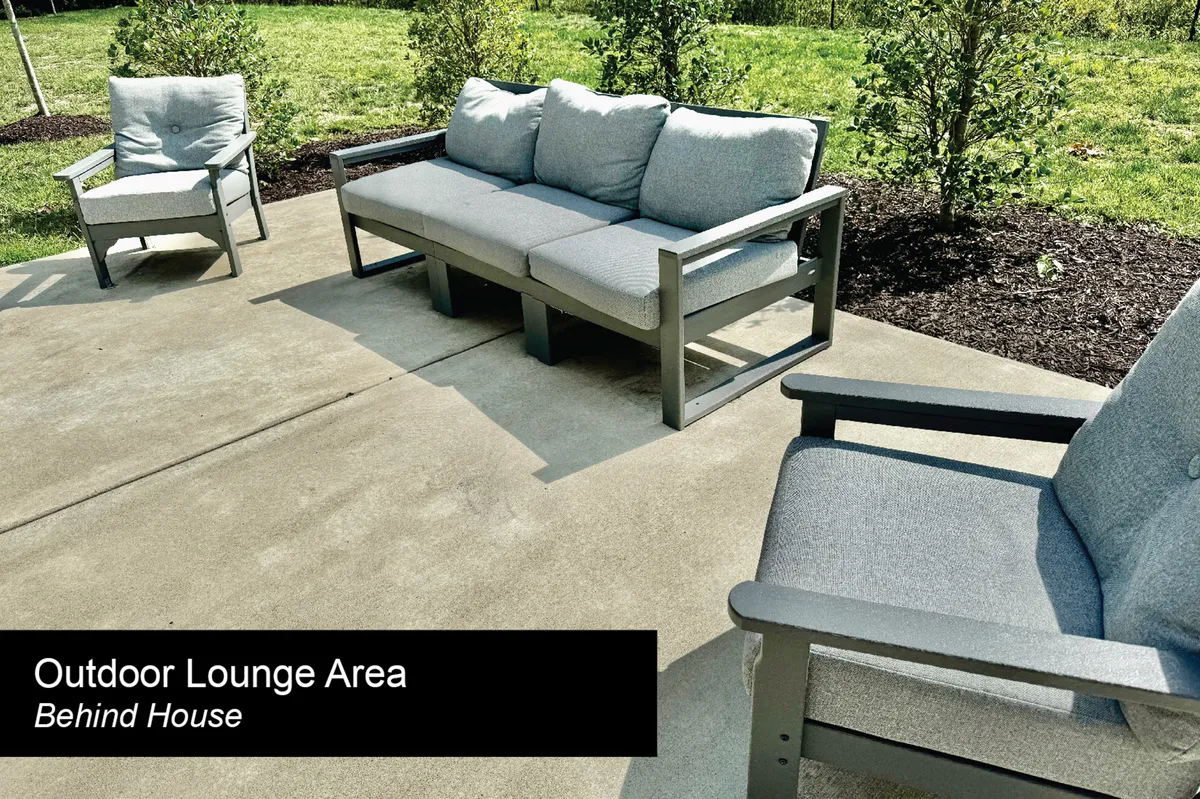 A tranquil exterior patio furnished with an outdoor sofa, accent chairs, and lush greenery, offering a comfortable setting to relax and unwind. The space is partially enclosed yet open to the fresh air.