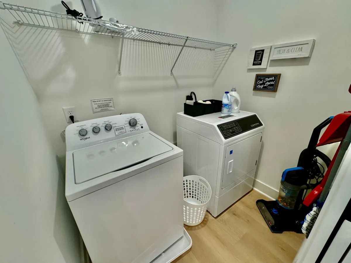 A well-organized laundry area with a washer and dryer, shelves holding supplies, and a laundry basket. The space is practical and tidy, offering convenience for extended stays or travel mishaps.