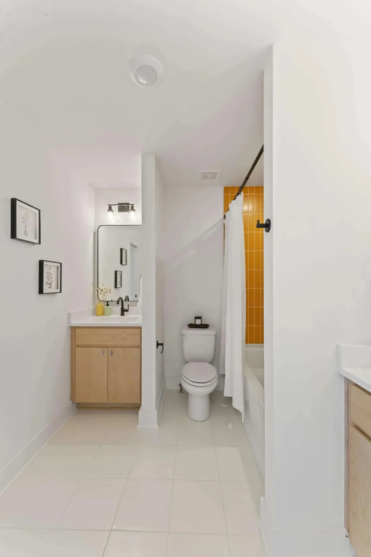 A modern, bright bathroom featuring a vanity, a distinct yellow tile wall, a shower area, and framed artwork. The space feels clean, stylish, and ready to accommodate multiple guests comfortably.