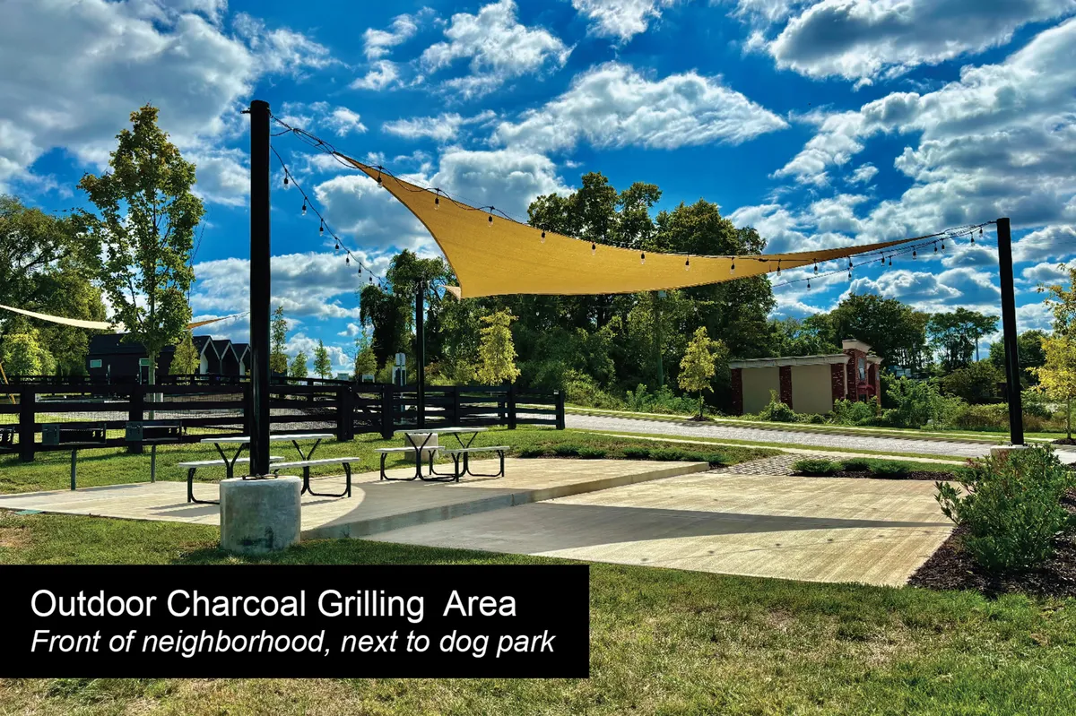 An inviting exterior communal area featuring a grilling section under a shade sail, picnic tables, and open green space. The scene subtly shows the area's suitability for both social gatherings and pet-friendly activities like dog walking.