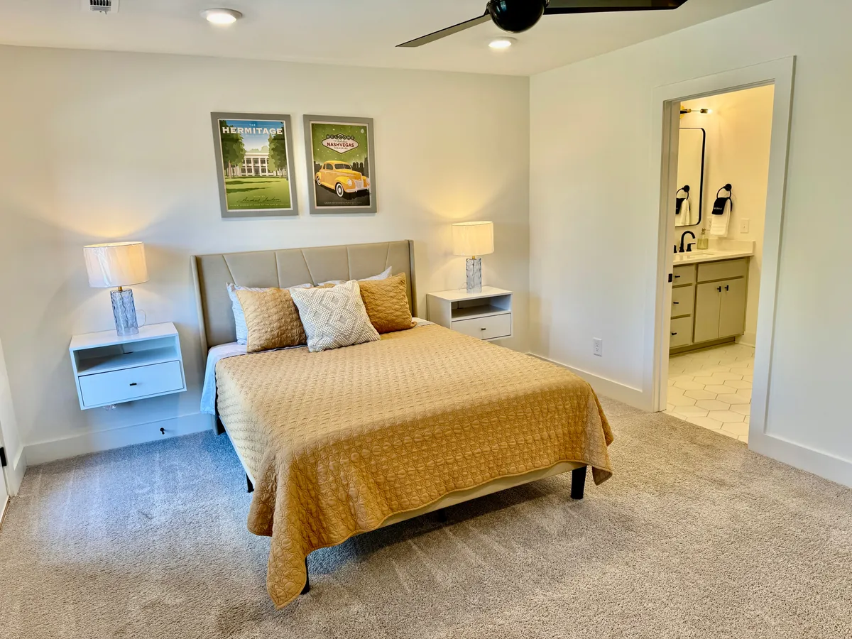 A serene bedroom with a comfortable bed, matching nightstands, and framed artwork above the headboard. Soft sunlight streams in, creating a peaceful atmosphere perfect for relaxation or reading.