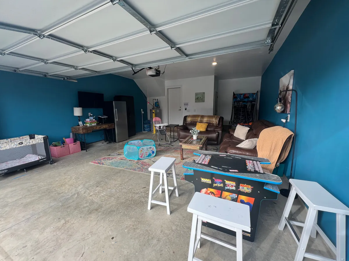 A cozy, playful interior featuring comfortable blue seating, a game table, and a decorative rug. The space is set up for relaxing, socializing, and friendly game nights—perfect for group activities after an evening out.